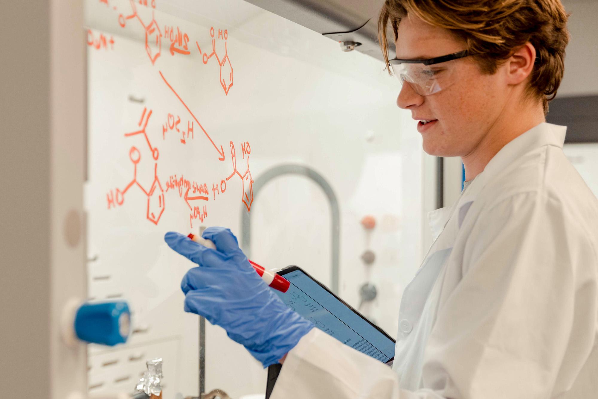 A student draws chemical diagrams on glass in a lab